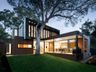 Modern home lit at dusk under a big shade tree
